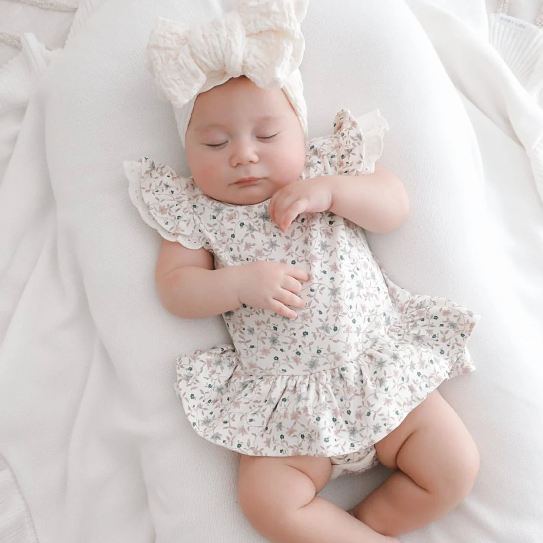 This winter floral onesie features long sleeves with flutter and lace detail over the shoulder, all over floral design with snap buttons to the neckline and bottom. A pretty design of tiny flowers and leaves in pastel pinks and blues…