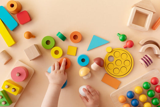 A toddler's hands engaging in sensory play with colourful wooden toys, including geometric shapes, blocks, and textured materials, promoting cognitive and motor skill development.